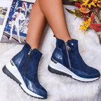 Bottines bleues en daim avec fermeture éclair, semelle épaisse blanche et détails en cuir texturé, posées sur un tapis avec magazine et décor automnal.