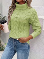 Femme portant un pull vert à col roulé torsadé, tenant un gobelet de café, avec un jean bleu. Mode automne, style décontracté, tendance féminine.