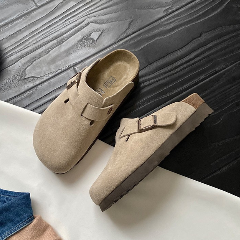 Sabots en daim beige sur sol en bois noir, design moderne avec boucle, semelle en liège. Chaussures confortables et tendance pour toutes saisons.