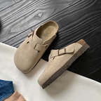 Sabots en daim beige sur sol en bois noir, design moderne avec boucle, semelle en liège. Chaussures confortables et tendance pour toutes saisons.
