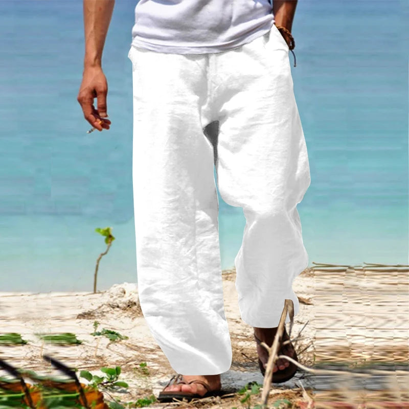 Homme en pantalon blanc en lin, marchant sur une plage ensoleillée, mer turquoise en arrière-plan, style décontracté estival, mode plage.