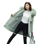 Femme portant un manteau d'hiver vert avec capuche en fausse fourrure, t-shirt blanc, jean noir déchiré, sac à main blanc. Mode hiver élégante.