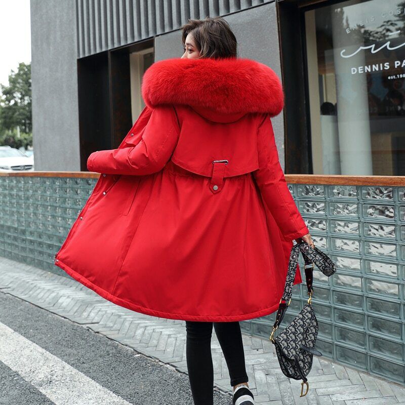 Femme portant un manteau rouge avec col en fourrure, tenant un sac à main, marchant en ville. Mode hiver élégante, tendance urbaine.