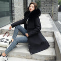 Femme en manteau noir avec col en fourrure, assise sur des marches en béton, portant un jean slim et des baskets blanches, sac blanc à côté.