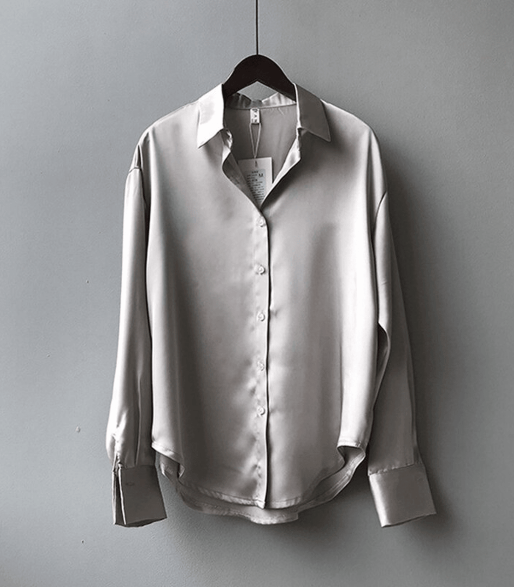 Chemise en soie grise élégante suspendue sur un cintre, manches longues, col classique, boutons discrets, style minimaliste, mode tendance.