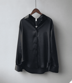 Chemise en satin noir suspendue sur un cintre en bois, manches longues, col classique, boutons noirs, style élégant et moderne.