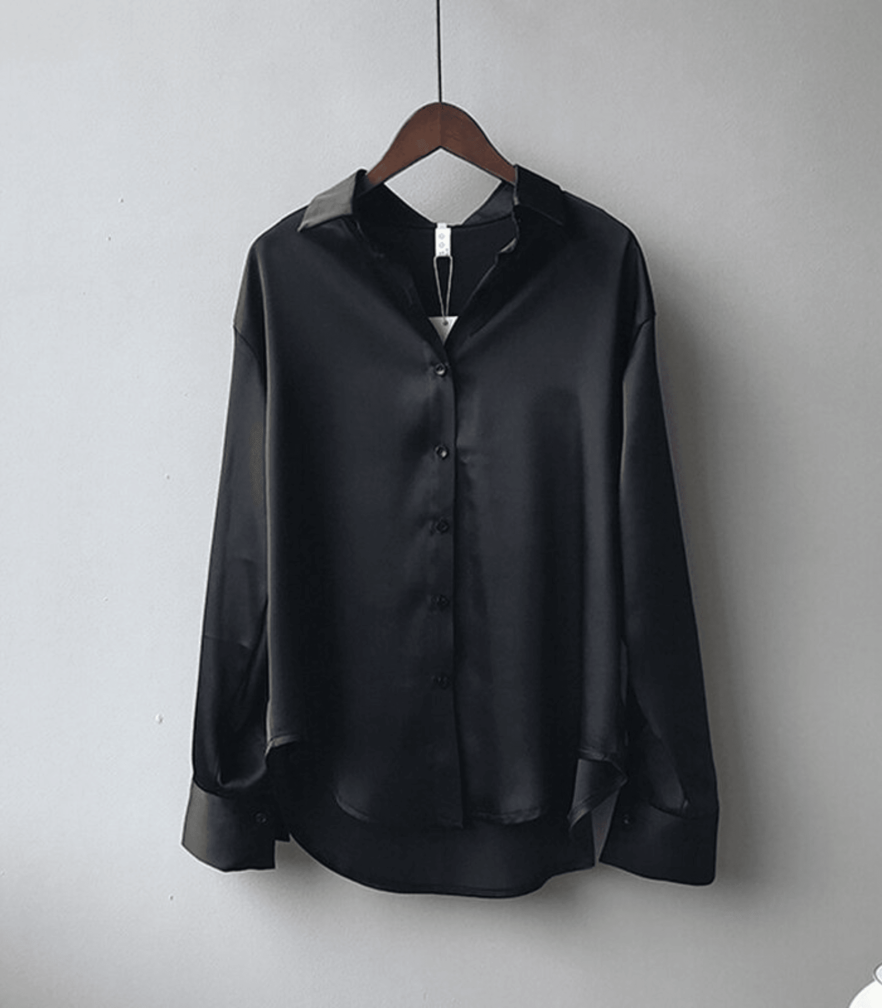 Chemise en satin noir suspendue sur un cintre en bois, manches longues, col classique, boutons noirs, style élégant et moderne.