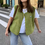 Femme portant un gilet vert en polaire sur un t-shirt blanc, posant dans une rue urbaine. Mode décontractée, tendance automne, style urbain.