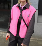 Femme portant un gilet rose vif en laine polaire sur une chemise noire, tenant un smartphone orange. Mode urbaine, tendance automne-hiver.