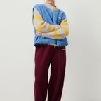Veste bleue en laine bouclée sur pull rayé jaune et gris, pantalon bordeaux. Mode automne-hiver, style décontracté et tendance.