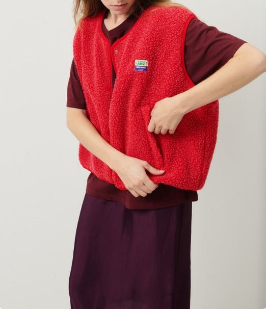 Femme portant un gilet rouge en laine bouclée, sur une robe bordeaux. Mode automne, style décontracté, tendance vêtements chauds.