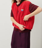 Femme portant un gilet rouge en laine bouclée, sur une robe bordeaux. Mode automne, style décontracté, tendance vêtements chauds.