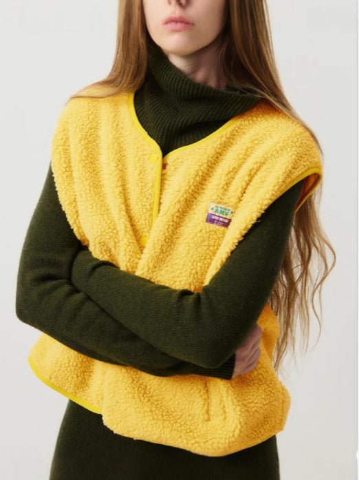 Femme portant un gilet en laine jaune sur un pull vert foncé à col roulé. Mode automne-hiver, style décontracté, tendance vêtements chauds.