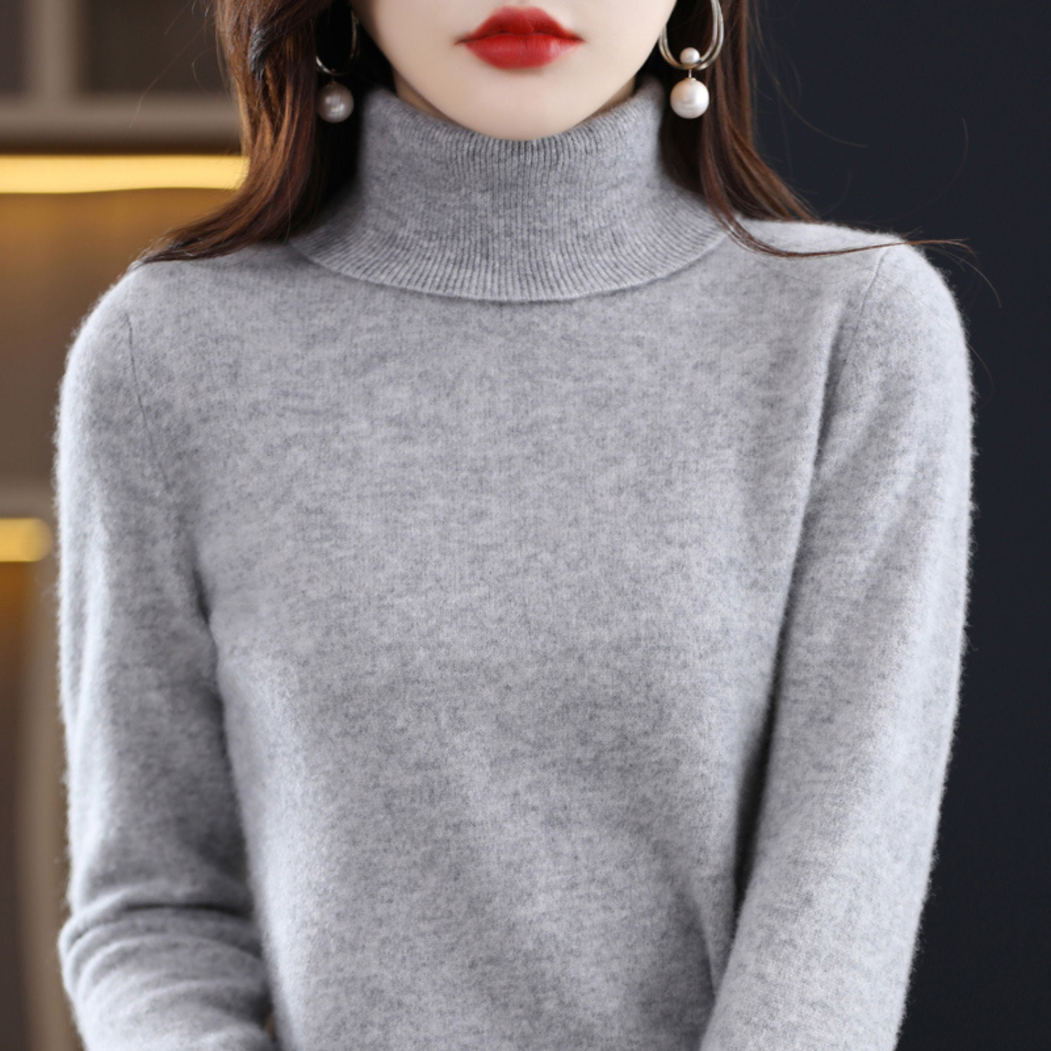 Femme portant un pull col roulé gris, boucles d'oreilles pendantes, lèvres rouges. Mode hiver élégante, style chic et moderne.