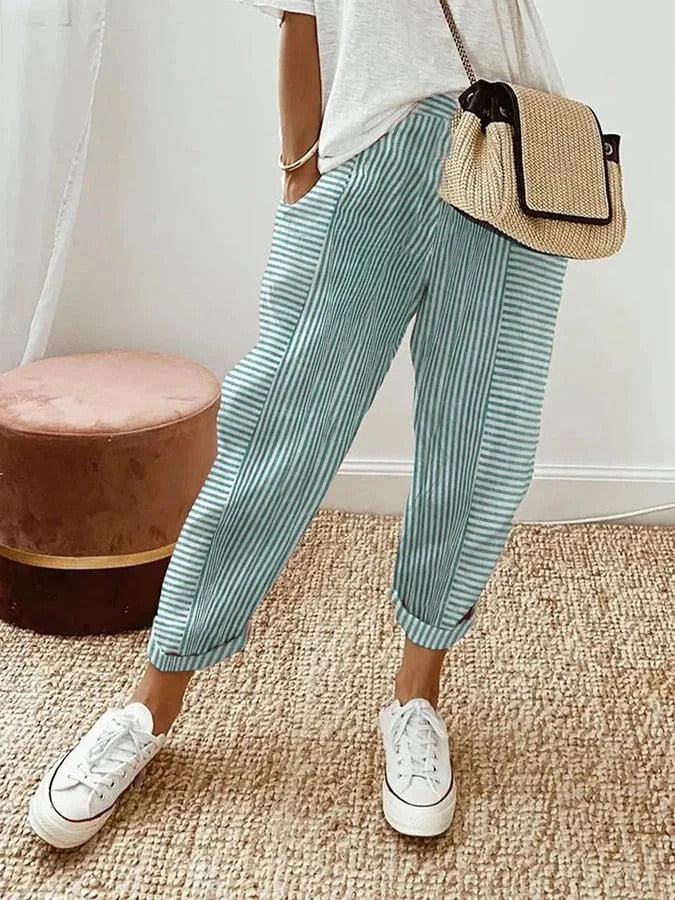Pantalon rayé bleu et blanc, porté avec un t-shirt blanc, baskets blanches et sac en osier. Mode décontractée, tendance estivale.