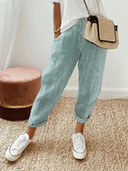 Pantalon rayé bleu et blanc, porté avec un t-shirt blanc, baskets blanches et sac en osier. Mode décontractée, tendance estivale.
