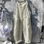 Salopette rayée beige suspendue sur un mur en béton, accompagnée d'un sac à dos blanc et de baskets blanches. Mode décontractée et tendance.