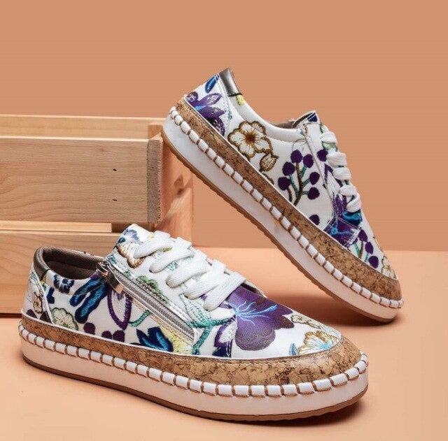 Baskets blanches à motifs floraux colorés, semelle en liège, posées sur fond beige avec boîte en bois. Chaussures tendance et écologiques.