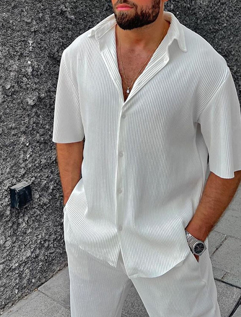 Homme portant une chemise blanche à manches courtes et un pantalon assorti, style décontracté, mode masculine élégante, montre-bracelet argentée.
