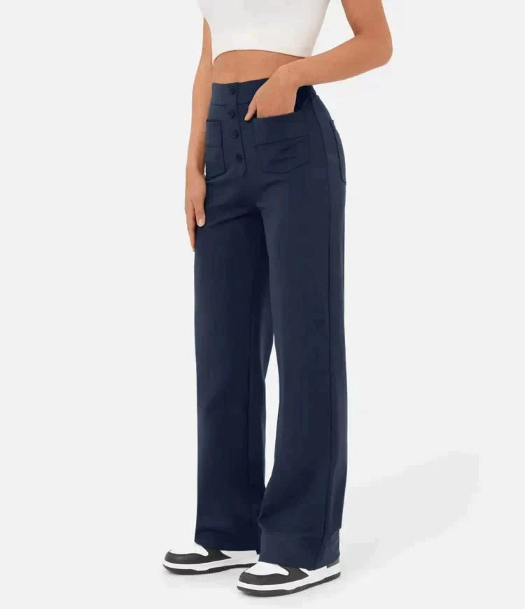 Femme portant un pantalon large bleu marine taille haute avec boutons, associé à un haut blanc court et des baskets noires et blanches.