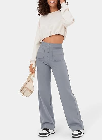 Femme souriante portant un pull court blanc et un pantalon large gris, tenant un petit sac beige, baskets noires et blanches. Mode décontractée tendance.