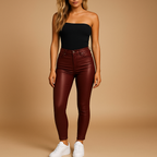 Femme portant un haut noir sans bretelles et un pantalon en cuir bordeaux, posant debout avec des baskets blanches sur fond beige.