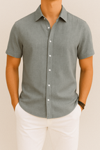 Chemise grise à manches courtes pour homme, élégante et moderne, avec boutons blancs, portée avec un pantalon blanc. Mode masculine chic et décontractée.