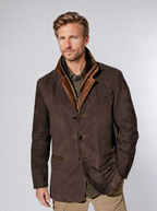 Homme portant une veste en cuir marron avec col en fourrure, chemise verte et pantalon beige. Mode masculine élégante, style automne-hiver.