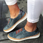Chaussures décontractées en cuir bleu pour femme, avec semelle blanche et détails colorés, portées avec un pantalon blanc. Mode, confort, style urbain.