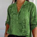 Chemisier vert à motifs floraux, manches retroussées, poche pailletée, col en V, porté avec colliers dorés. Mode élégante et tendance.