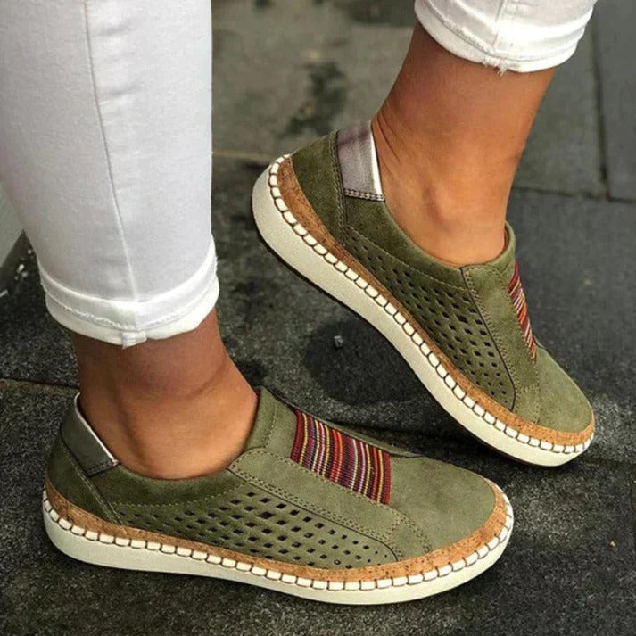 Chaussures décontractées vertes pour femmes avec motifs colorés, semelle blanche et détails perforés, portées avec un pantalon blanc.