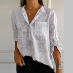Chemisier blanc à motifs floraux, manches retroussées, poche poitrine, porté avec des colliers dorés. Mode féminine élégante et décontractée.