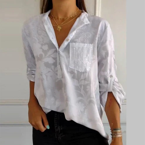 Chemisier blanc à motifs floraux, manches retroussées, poche poitrine, porté avec des colliers dorés. Mode féminine élégante et décontractée.