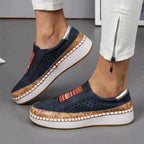 Chaussures compensées bleu marine avec semelle en liège, détails perforés et bandes colorées, portées avec un pantalon blanc zippé.