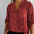 Chemisier rouge à motifs floraux, manches retroussées, poche pailletée, col en V, porté avec collier doré. Mode féminine élégante et tendance.