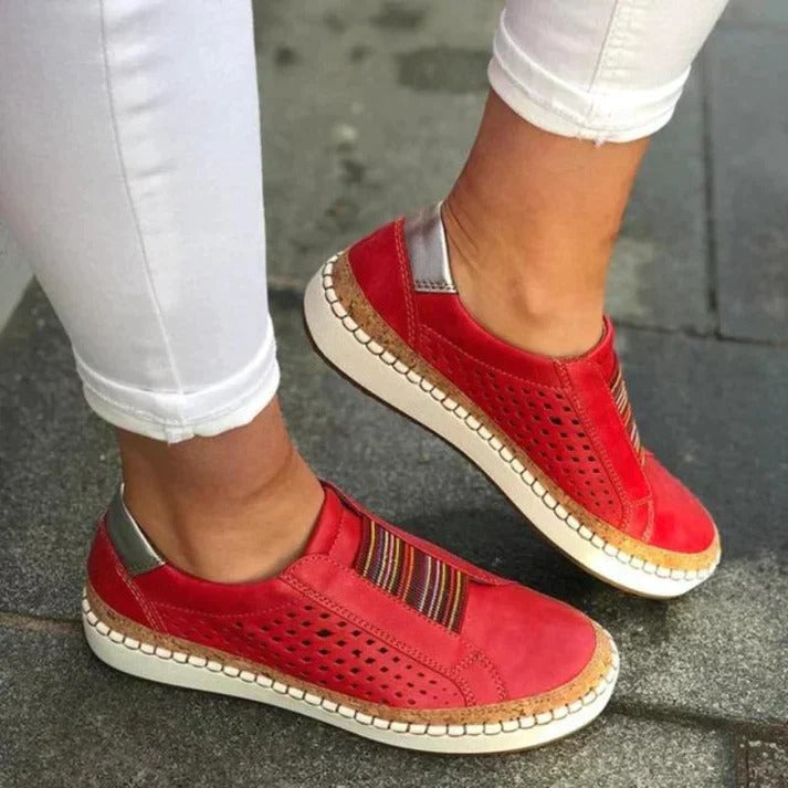 Chaussures rouges en cuir perforé pour femme, semelle blanche, détails multicolores, portées avec un pantalon blanc. Mode, confort, style urbain.