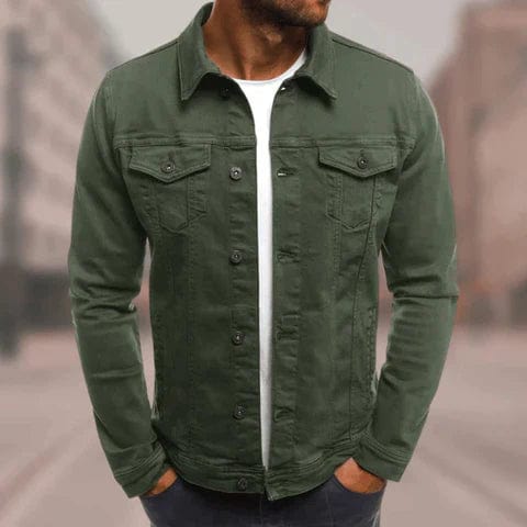 Homme portant une veste en jean verte, style décontracté, sur un t-shirt blanc, dans un environnement urbain flou. Mode masculine tendance.