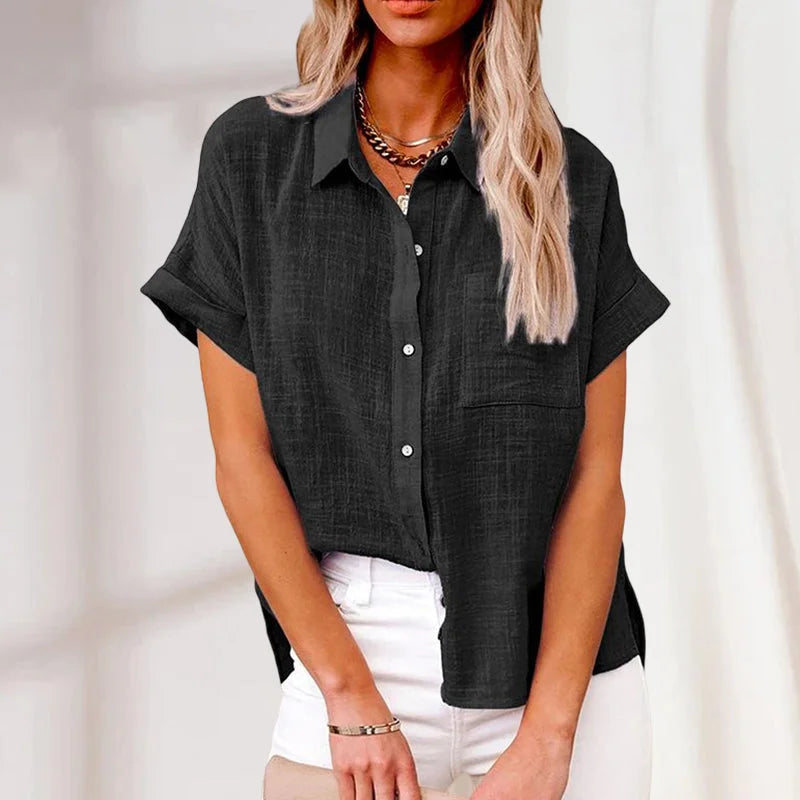 Femme portant une chemise noire en lin à manches courtes, col classique et boutons, associée à un pantalon blanc. Mode élégante et décontractée.