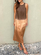 Robe longue dégradée marron et beige, sans manches, portée par une femme. Mode estivale élégante, sandales plates, mur texturé en arrière-plan.