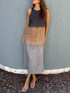 Robe longue dégradée femme, sans manches, tons noir, marron et gris, portée avec sandales dorées, devant un mur texturé gris.