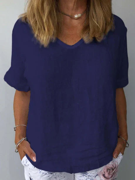 Femme portant un t-shirt bleu marine à col en V, manches courtes, avec un collier et un pantalon blanc à motif floral. Mode décontractée élégante.
