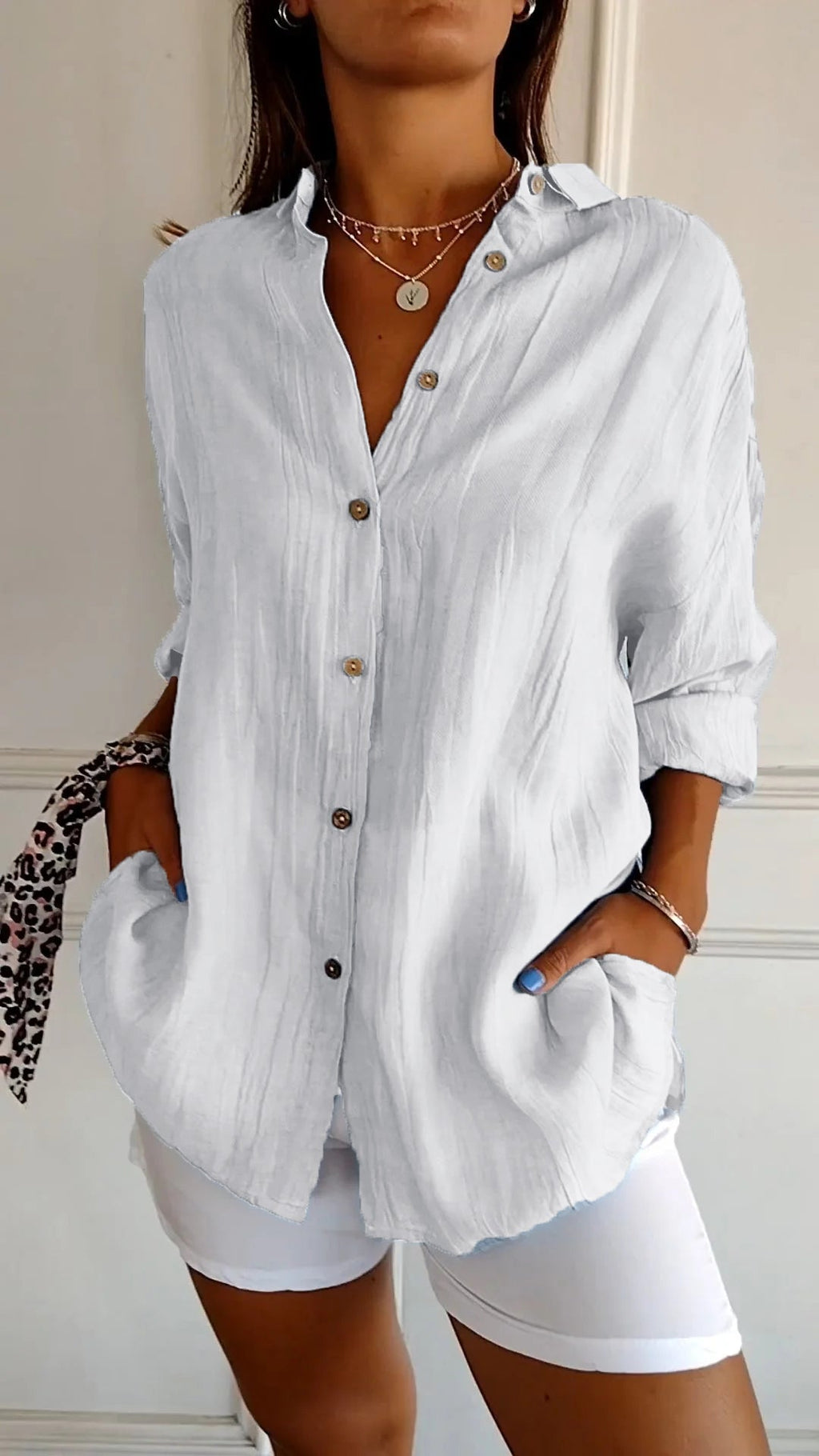 Femme portant une chemise blanche en lin avec boutons en bois, manches retroussées, associée à un pantalon blanc. Style décontracté et élégant.