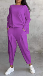 Femme portant un ensemble violet ample avec des poches, composé d'un haut à manches longues et d'un pantalon, assorti de baskets blanches.