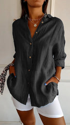Femme portant une chemise noire ample à manches longues avec boutons, associée à un pantalon blanc. Style décontracté chic, mode féminine tendance.