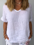 Femme portant un t-shirt en lin blanc, manches courtes, col en V, avec un collier perle. Mode estivale décontractée, tendance et élégante.