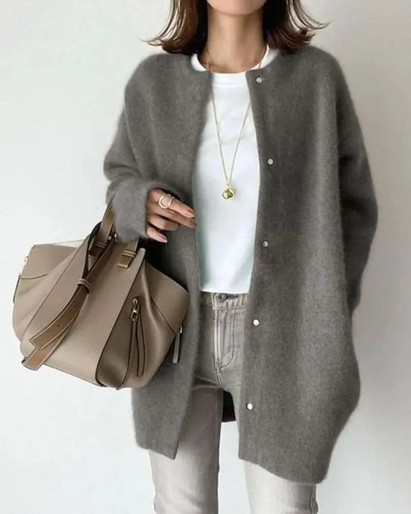 Femme portant un cardigan gris en laine, t-shirt blanc, jean clair, collier doré, et sac à main beige. Mode automne-hiver élégante et décontractée.