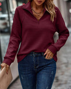 Femme portant un pull bordeaux à col zippé, manches longues, associé à un jean bleu. Mode automne, style décontracté, rue urbaine.