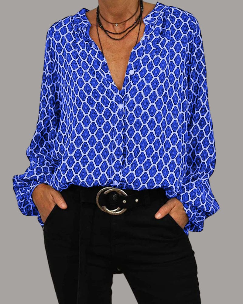 Chemisier bleu à motifs géométriques, col en V, manches longues, porté avec un pantalon noir et ceinture à boucle ronde. Mode féminine élégante.