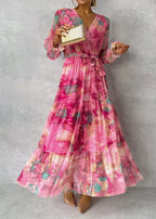 Robe longue rose à motifs floraux, manches longues, ceinture à nouer, tenue élégante pour soirée, femme tenant une pochette dorée.
