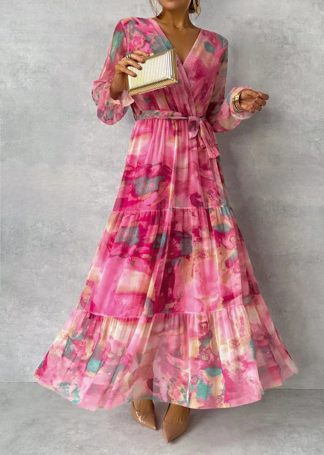 Robe longue rose à motifs floraux, manches longues, ceinture à nouer, tenue élégante pour soirée, femme tenant une pochette dorée.